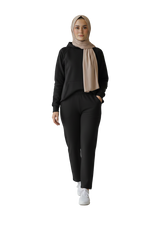 Person wearing a black outfit with a beige hijab on a plain background