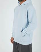 Man wearing a light blue hoodie and gray pants on a white background