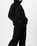 Person wearing a black hoodie and pants on a white background