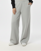 Woman wearing a black sweater and light gray pants on a white background